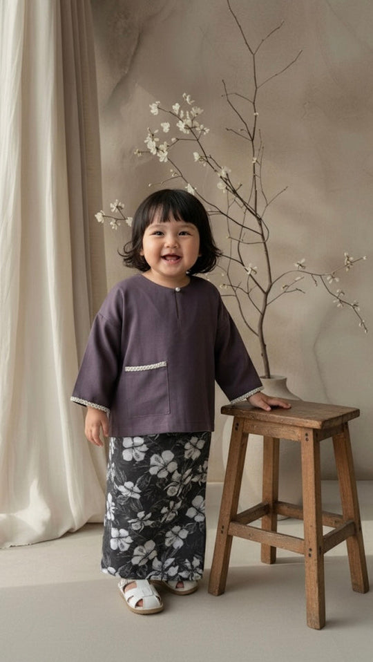 Child standing next to a wooden stool with a branch and white flowers in the background