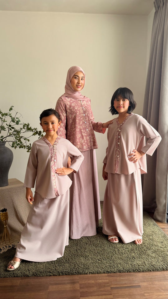 Three women in matching pink and gray traditional outfits standing indoors.