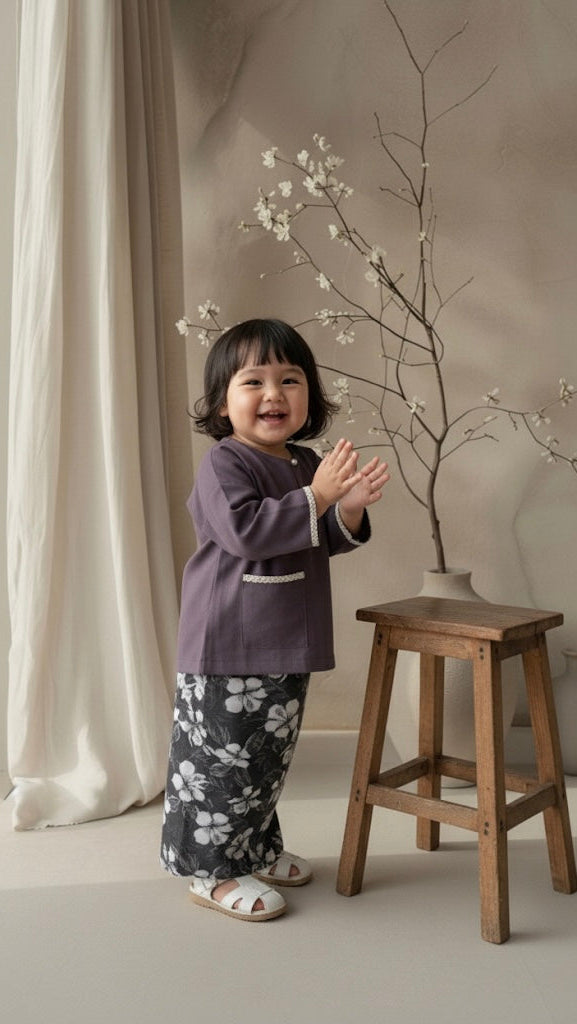 Child standing next to a wooden stool with a branch and white flowers in a neutral setting