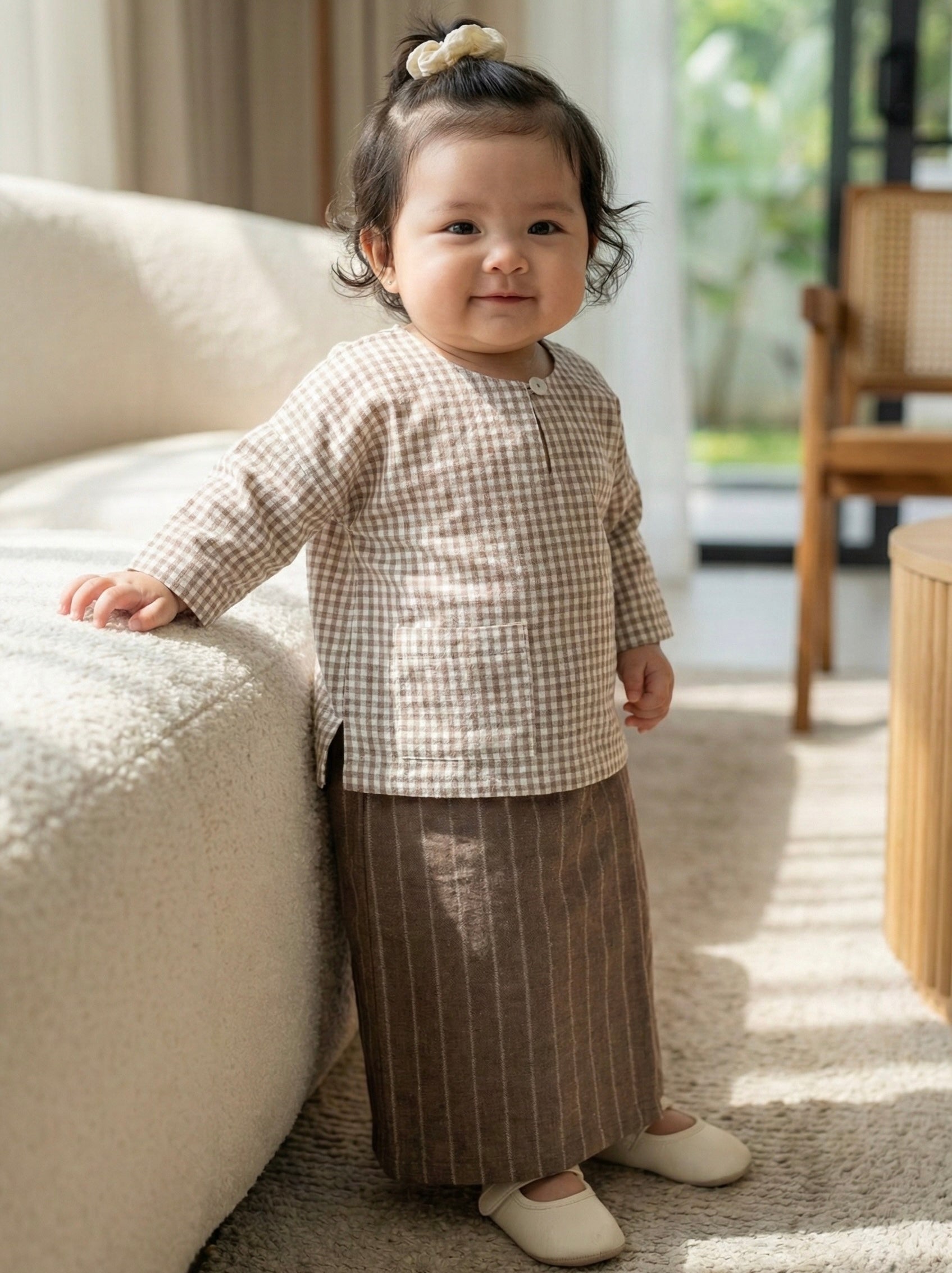 Child wearing a checkered shirt and striped pants standing in a living room.