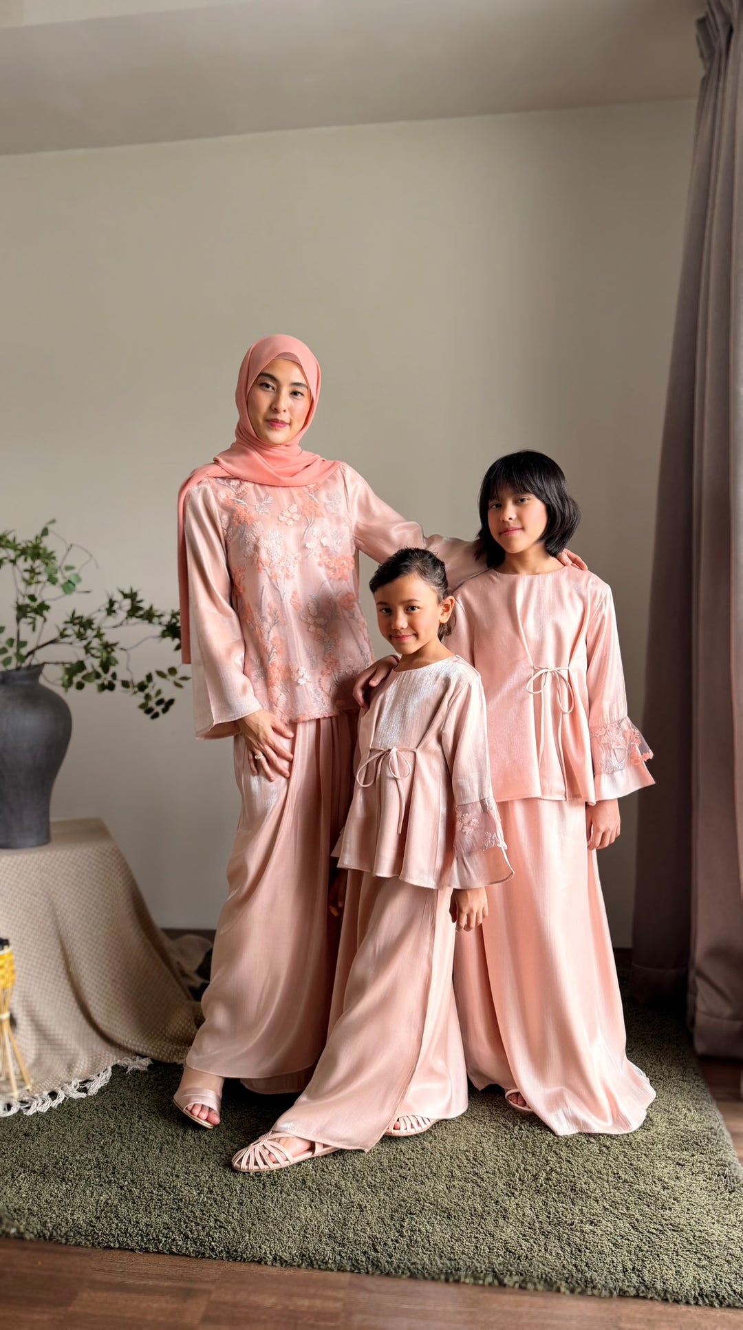 Three women in matching pink traditional outfits standing indoors.