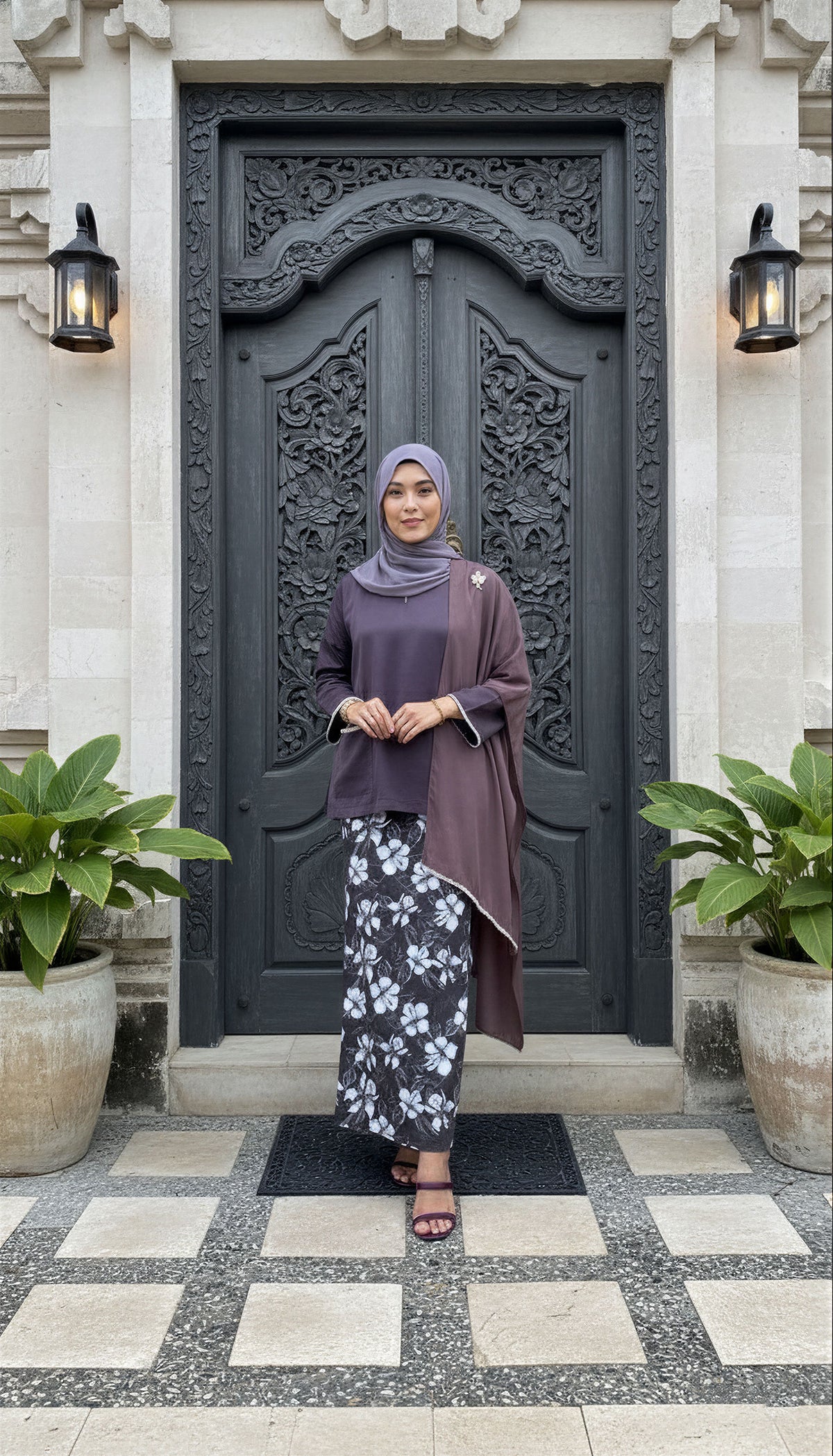 Woman standing in front of a ornate black door with plants on either side.